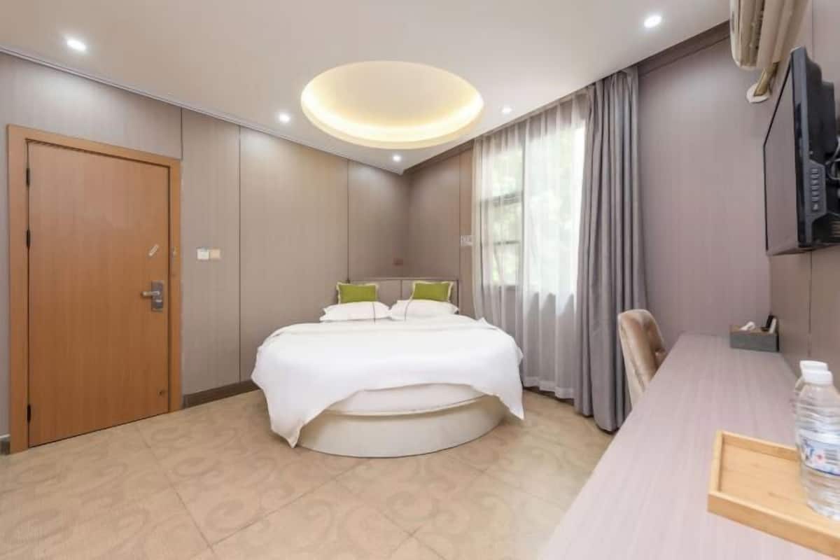A hotel room with a bed, a desk, a chair, a TV, and a door.