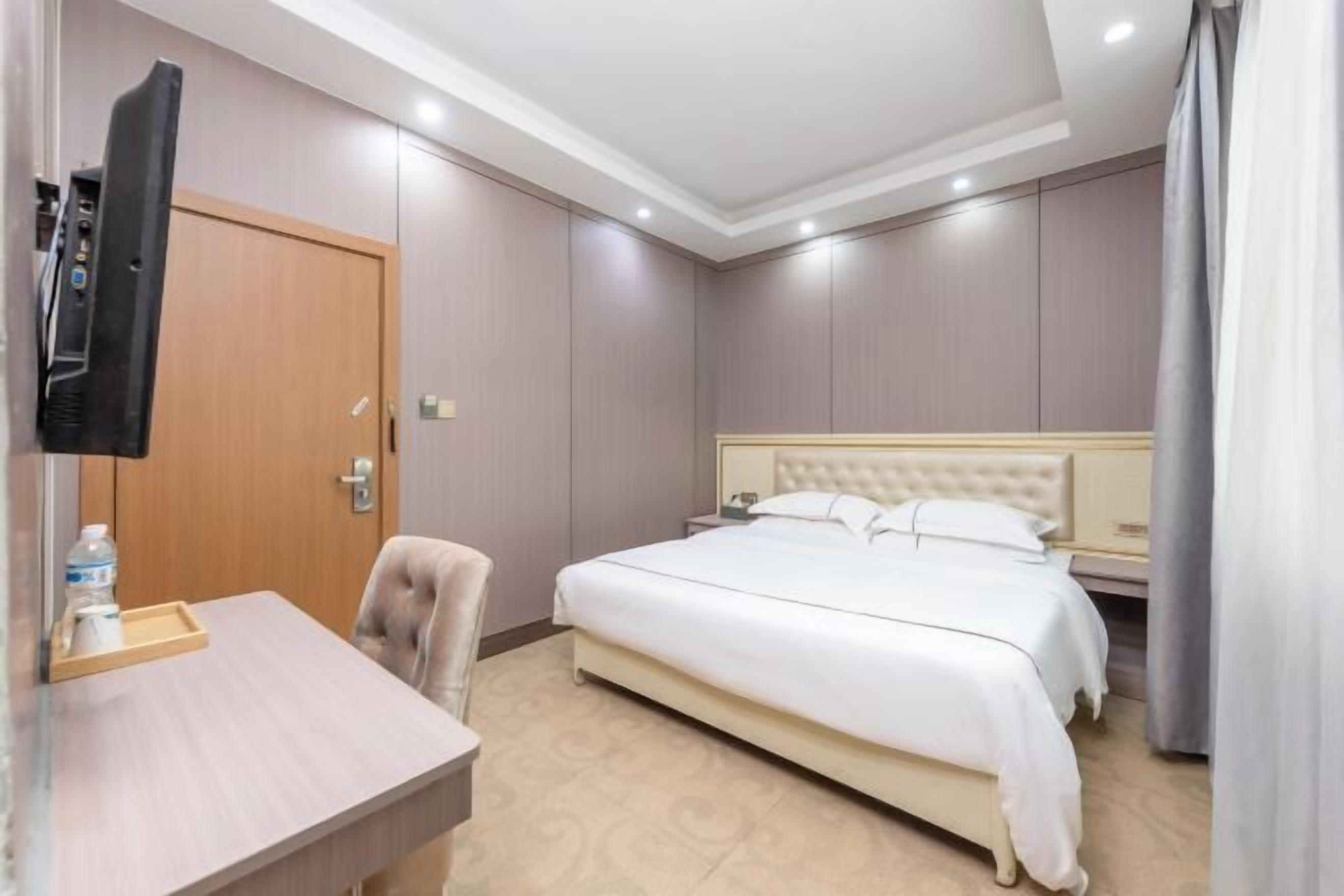 A hotel room with a bed, a desk with a chair, a TV, and a door.