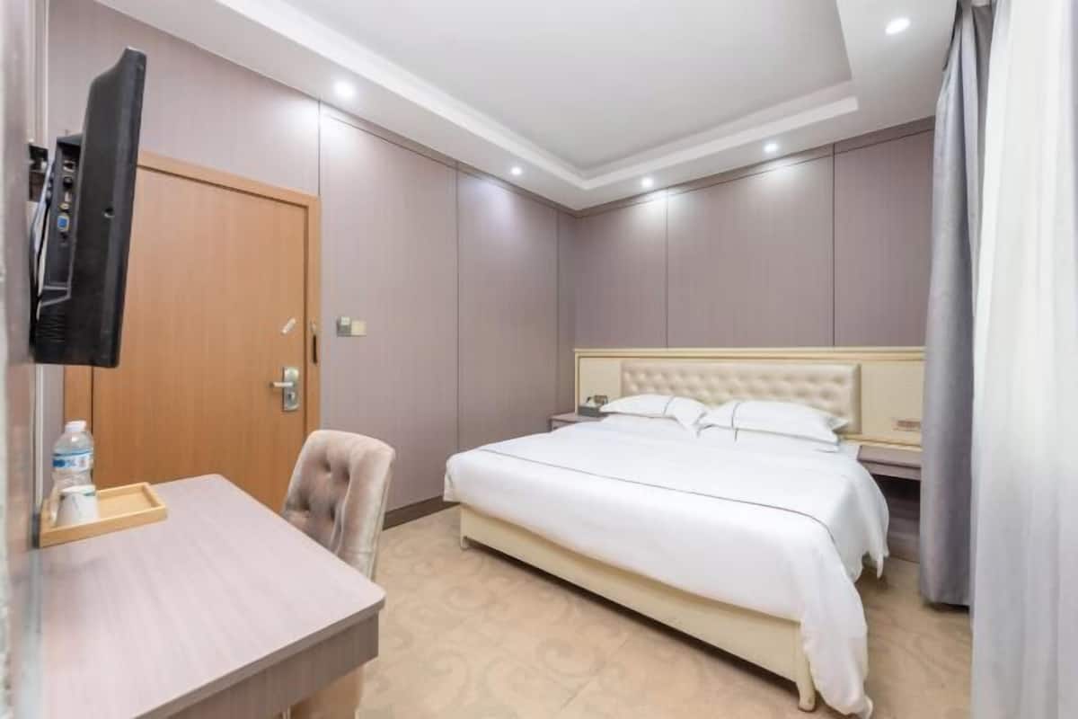 A hotel room with a bed, a desk with a chair, a TV, and a door.