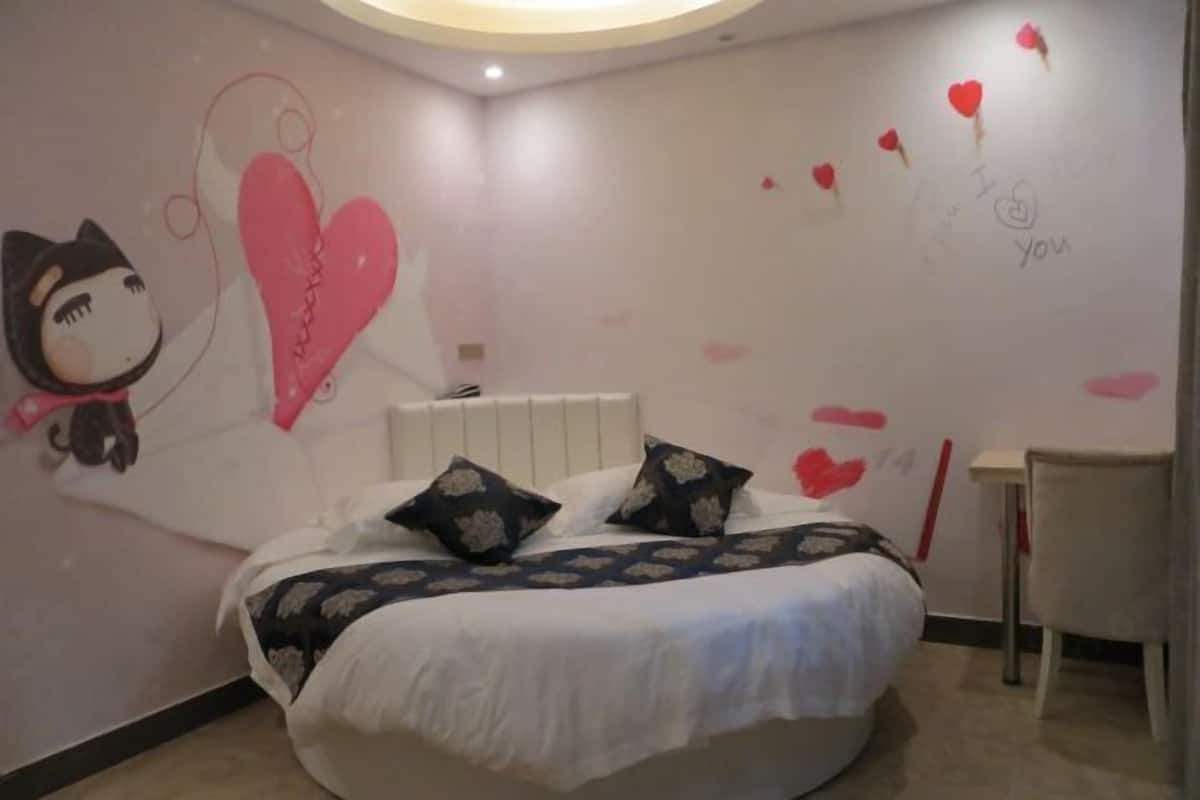 A bedroom with a bed, pillows, a chair, and a wall with heart decorations and a cat illustration.