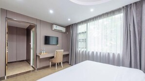 Quarto de hotel com cama, escrivaninha, cadeira, televisão e janela com cortinas.