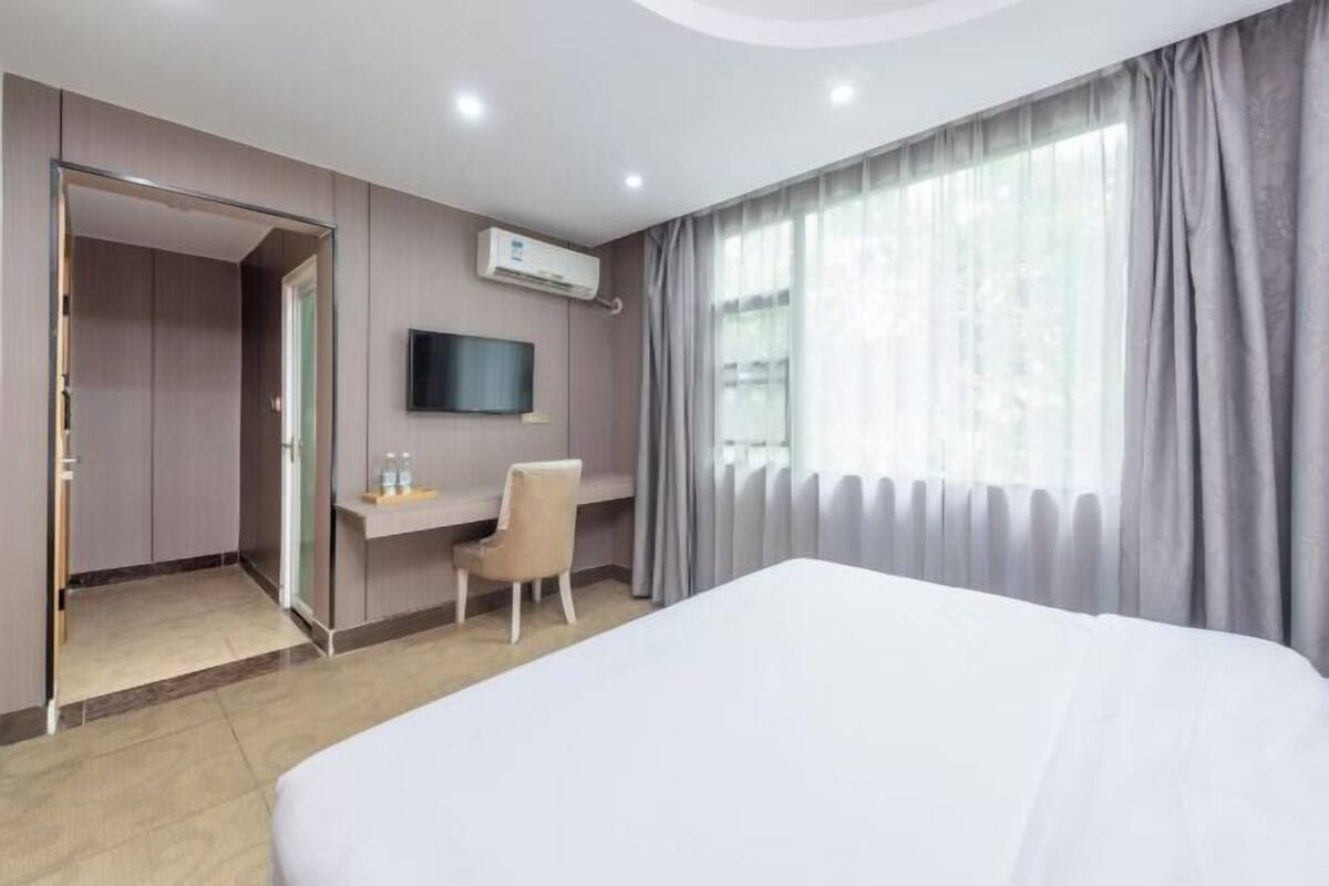 A hotel room with a bed, a desk, a chair, a TV, and a window with curtains.