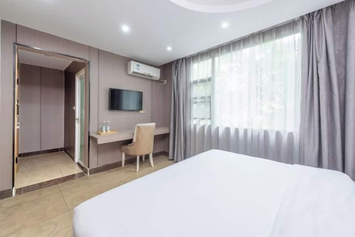 A hotel room with a bed, a desk, a chair, a TV, and a window with curtains.
