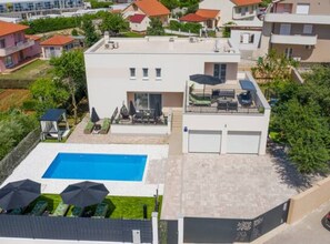 A modern two-story house with a swimming pool, outdoor seating, and a garage.