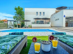 A poolside area with lounge chairs, a table with drinks, and a building in the background.