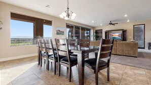 A spacious dining area with a large table and chairs, a ceiling fan, and large windows offering a view of the outdoors. - Luxury Desert Playground: Golf View + Resort Access (Hurricane)