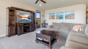 A living room with a flat-screen TV, a wooden coffee table, a sofa, and a ceiling fan. - Luxury Desert Playground: Golf View + Resort Access (Hurricane)
