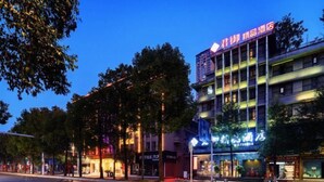 Un hôtel à plusieurs étages, doté d'une enseigne lumineuse et situé sur une rue bien éclairée au premier plan.