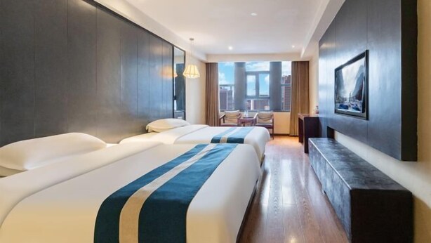 Ein Hotelzimmer mit zwei Betten, einer Sitzecke mit Blick und einem an der Wand befestigten Fernseher.