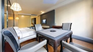 Ein modernes Hotelzimmer mit Essbereich, inklusive Tisch, Stühlen, Fernseher und Deckenleuchte.