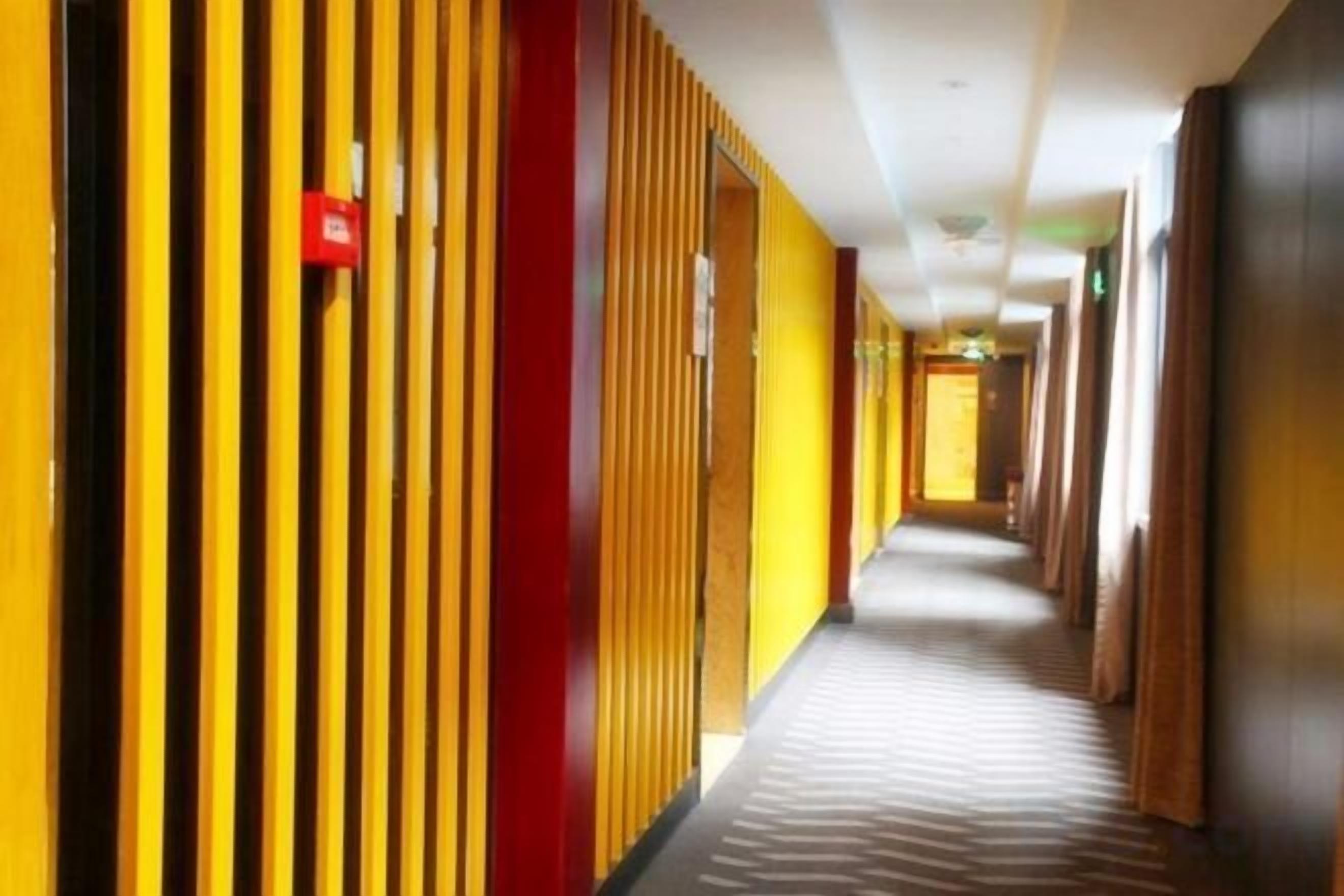 A hotel corridor with vertical wooden slats on the walls, a carpeted floor, and doors leading to rooms.