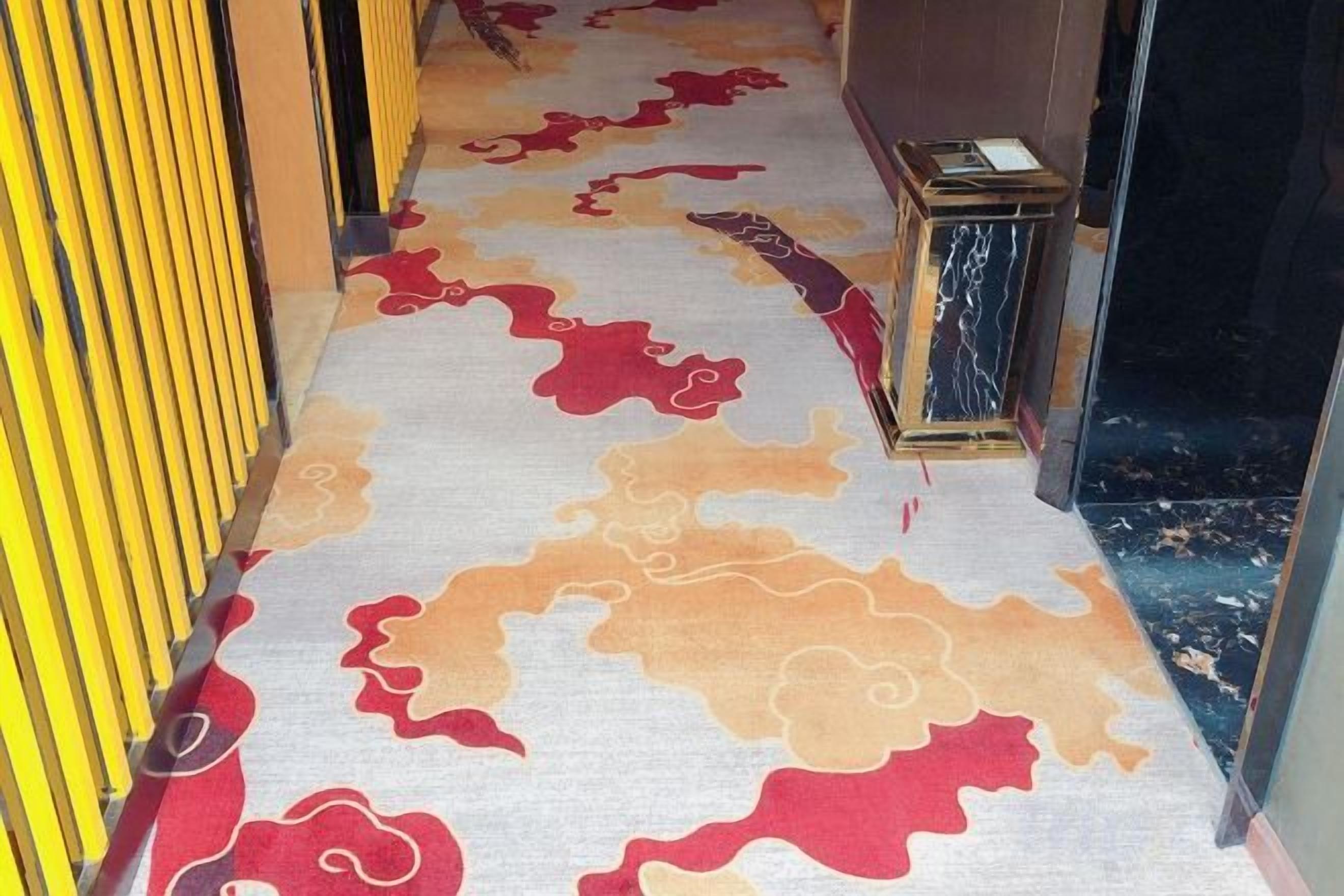 A carpeted hallway with a patterned design, a yellow wall, and a door leading to a room.