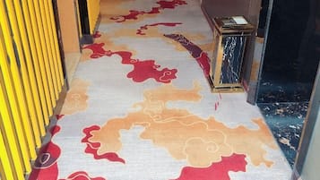 A carpeted hallway with a patterned design, a yellow wall, and a door leading to a room.
