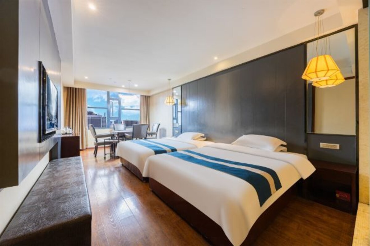 Een hotelkamer met twee bedden, een bureau, een stoel, een televisie en een groot raam.