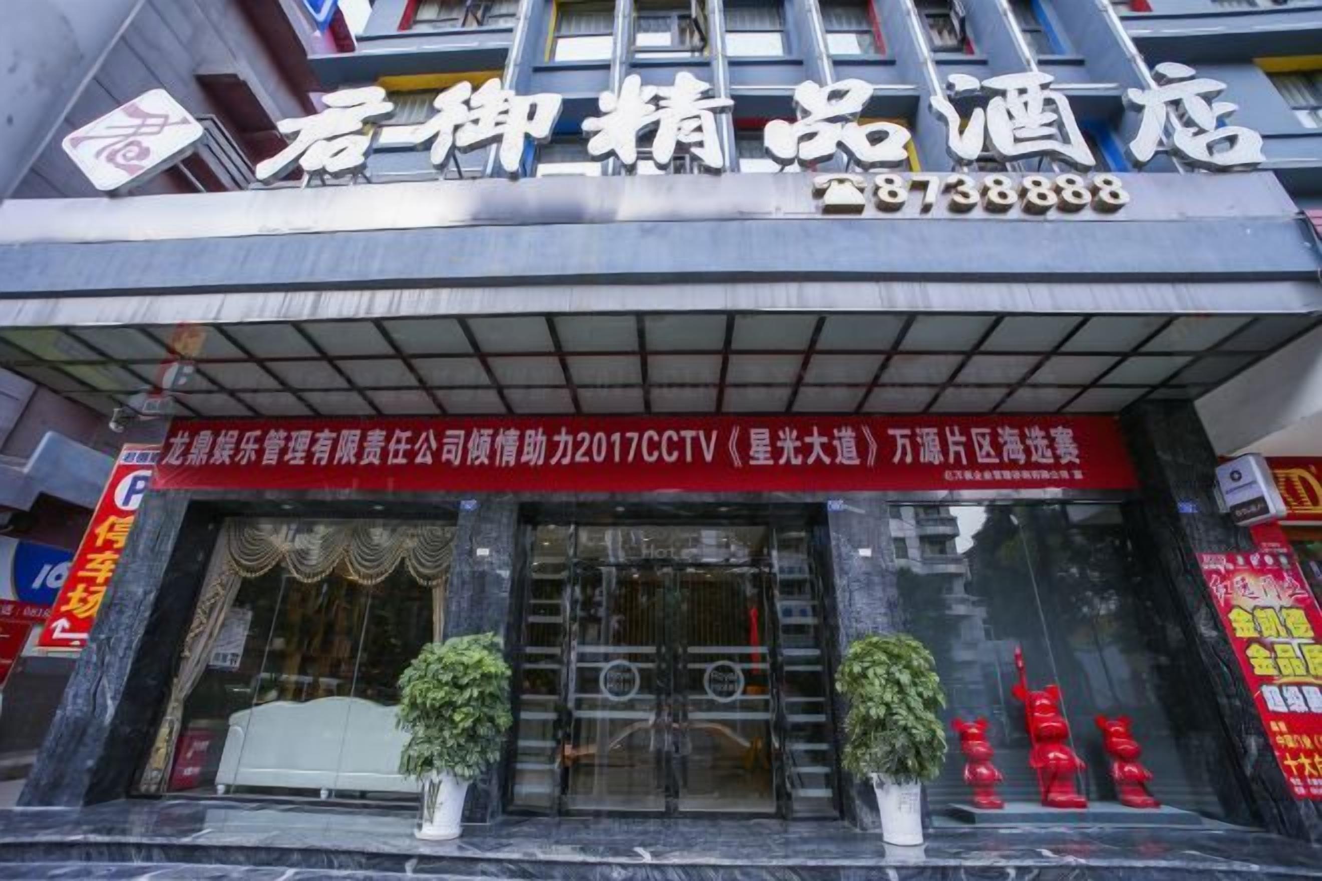 A hotel entrance with a signboard, potted plants, and a red banner.