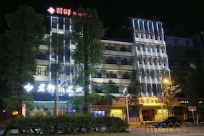 A multi-story building with illuminated signage, a visible entrance, and a parking area. - Junyu Boutique Hotel (Wanyuan Railway Station) (Wanyuan)
