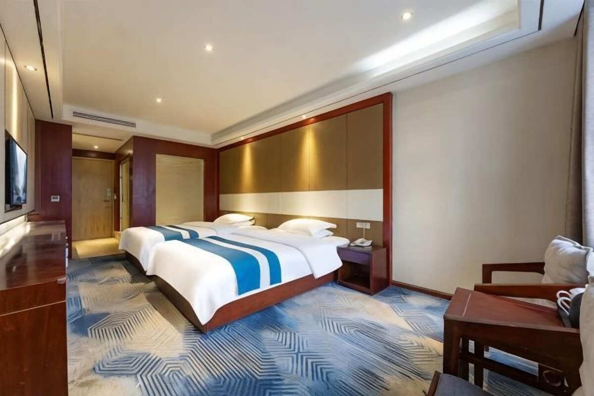 A hotel room with a large bed, a desk, a chair, a TV, and a large window.