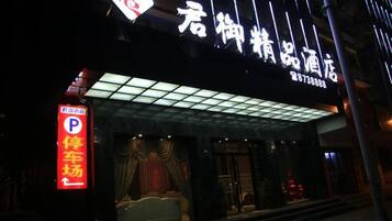 A hotel entrance with a neon sign, a parking sign, and a covered entrance area.