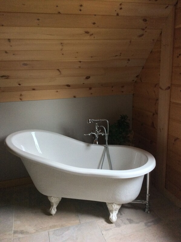 A freestanding bathtub in a room with wooden walls and a tiled floor.
