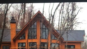 A large, multi-story log cabin with a prominent chimney, large windows, and a stone foundation. - Cottage life in Quebec  (Morin-Heights)