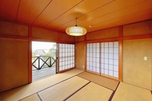 A traditional Japanese room with tatami flooring, sliding doors, and a hanging light fixture. - Vacation Rental Shirayuri (Ito)