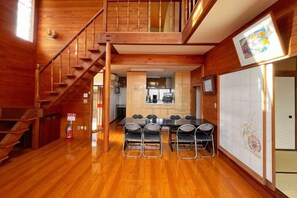 A wooden interior with a staircase, a dining area with chairs, and a kitchen in the background. - Vacation Rental Shirayuri (Ito)