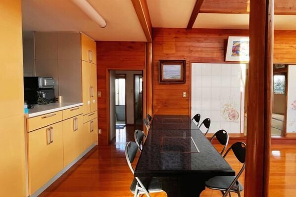 A long dining table with chairs, wooden cabinets, and a kitchen area with appliances. - Vacation Rental Shirayuri (Ito)