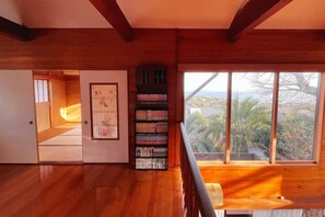 A wooden interior with a bookshelf, a sliding door, and a view through large windows. - Vacation Rental Shirayuri (Ito)