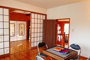 A traditional Japanese room with tatami flooring, a sliding door, and a table with books. - Vacation Rental Shirayuri (Ito)