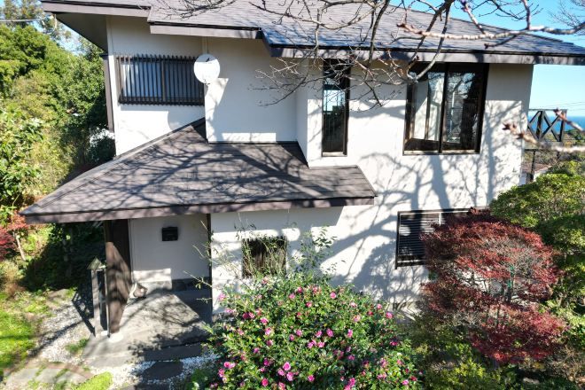 A two-story house with a sloped roof, a small porch, and a garden with flowering plants.
