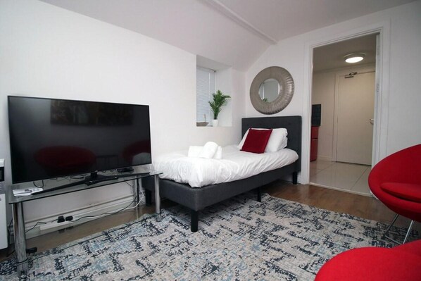 A modern bedroom with a bed, a TV, a desk, and a red chair. - 5 Bed House - Sleeps 16 - Parking - Wifi (Swansea)