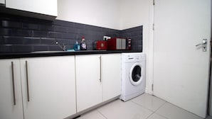 A compact kitchen with white cabinets, a black tiled backsplash, a washing machine, and a red appliance on the countertop. - 5 Bed House - Sleeps 16 - Parking - Wifi (Swansea)