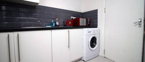 Una cocina compacta con armarios blancos, un salpicadero de azulejos negros, una lavadora y un electrodoméstico rojo en la encimera.