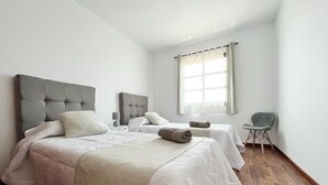 Camera da letto moderna con due letti, una testiera grigia imbottita, un comodino con una lampada e una finestra con tende.