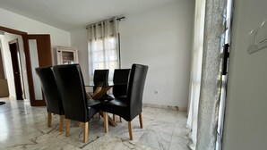 Zona pranzo con tavolo in vetro, sedie nere, parete bianca e pavimento in marmo.