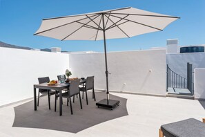 A patio with a table set for two, a large umbrella, and a portable heater.