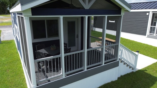 A covered patio area with a table and chairs, a small staircase leading up to the entrance, and a view of the surrounding lawn and buildings. - Lake View Cabin, 20 miles from New Bern! (Maysville)