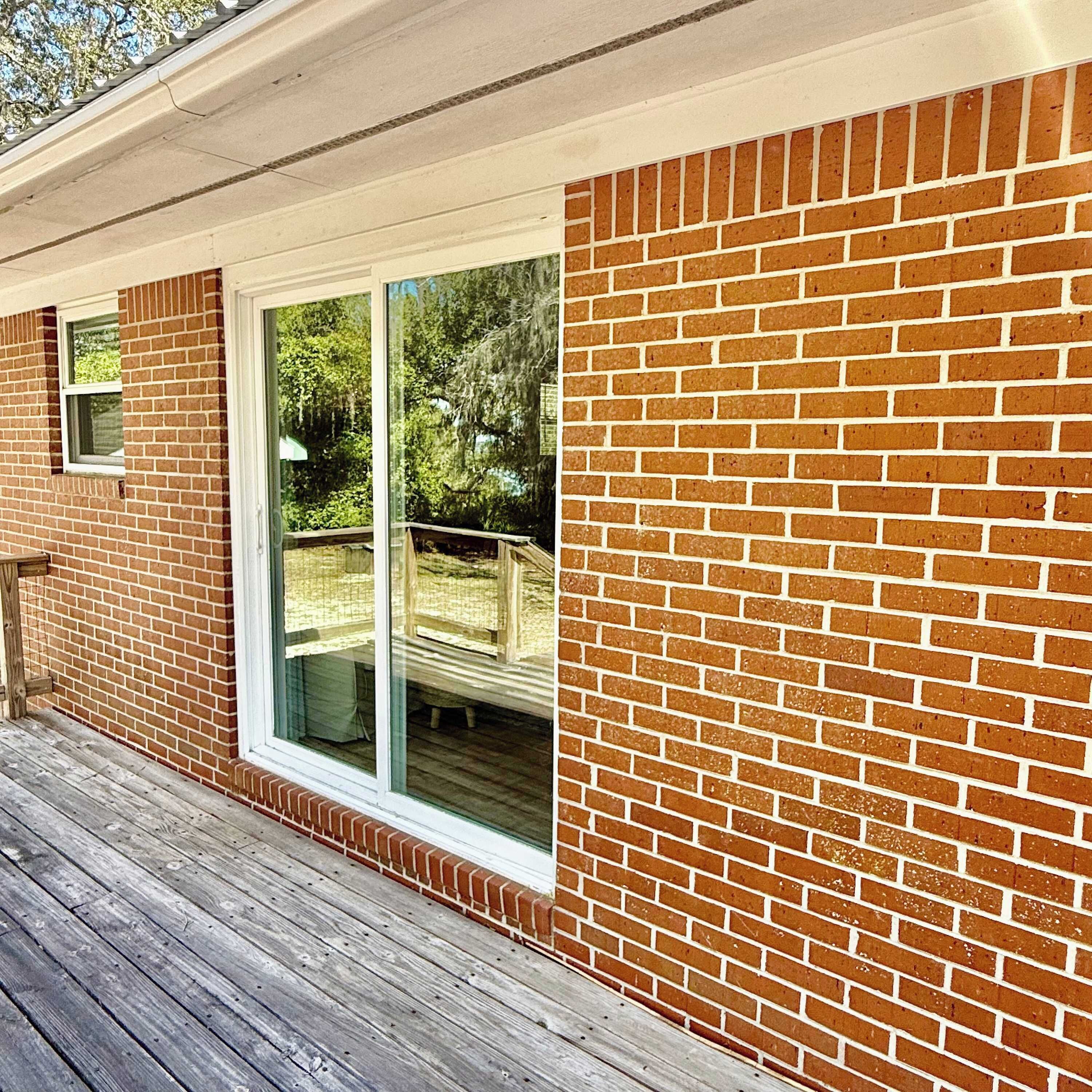 A brick exterior with a large sliding glass door, a wooden deck, and a small window.