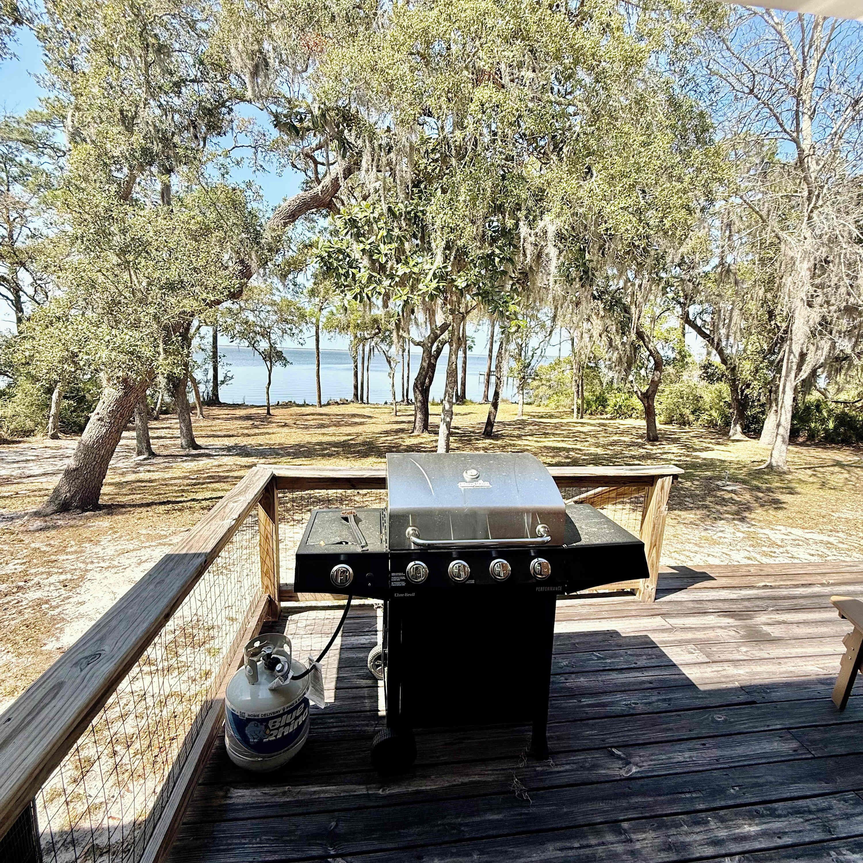Ein Grill auf einer Holzterrasse mit Blick auf einen See und Bäume.