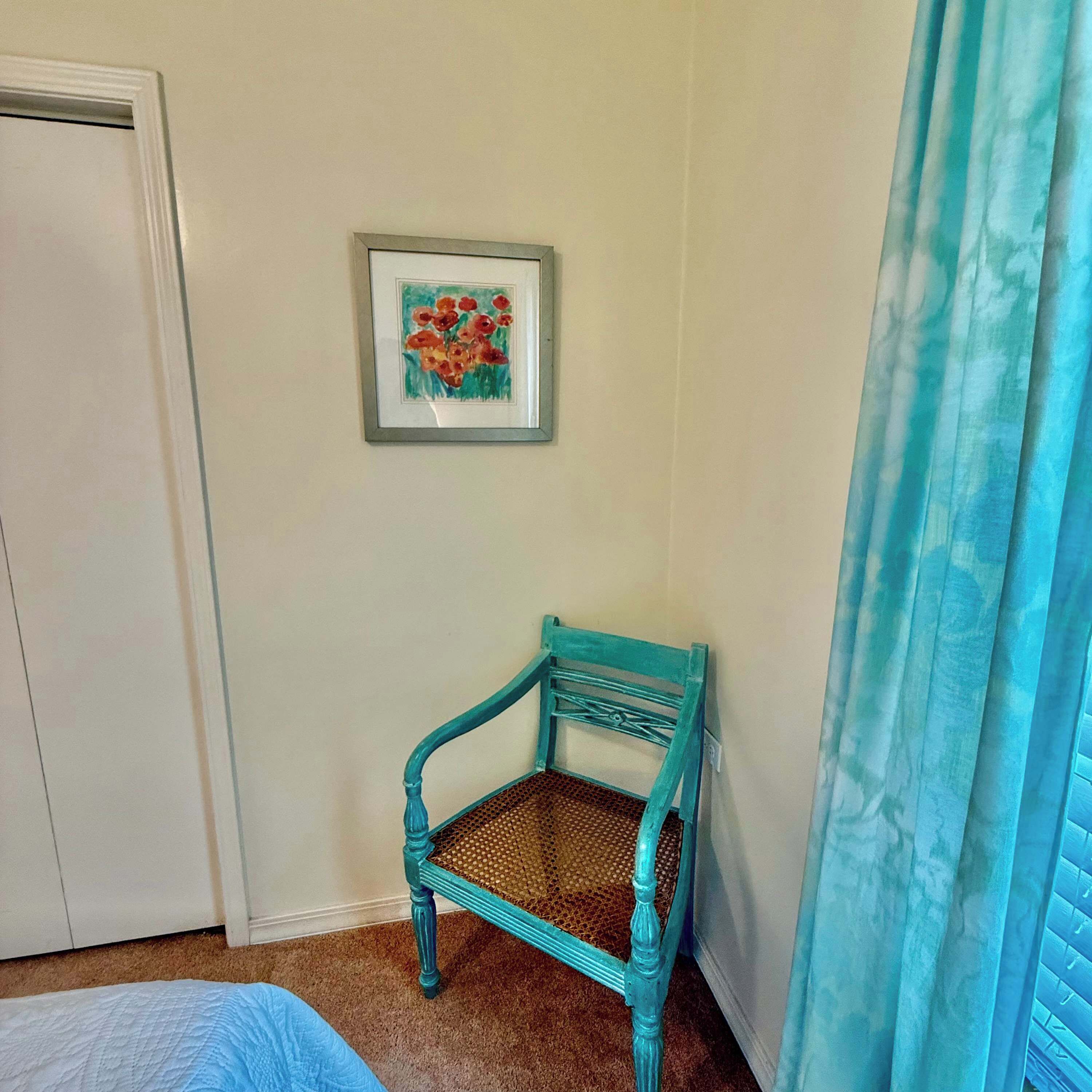 Una habitación con una silla color turquesa, un cuadro enmarcado, una puerta y una cortina.