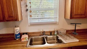 Een keuken met houten kastjes, een dubbele spoelbak, een raam met zonwering en een hangrek.