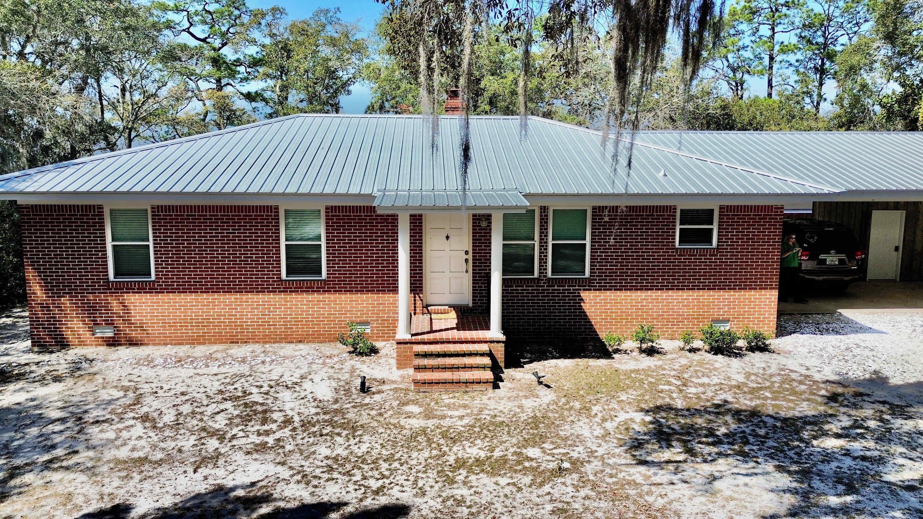 A single-story brick house with a metal roof, a front porch, and a garage.