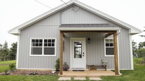 Ein eingeschossiges Haus mit Veranda, einer weißen Tür und zwei Fenstern an der Seite.