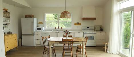 A spacious kitchen with a large dining table, wooden chairs, and a hanging light fixture.