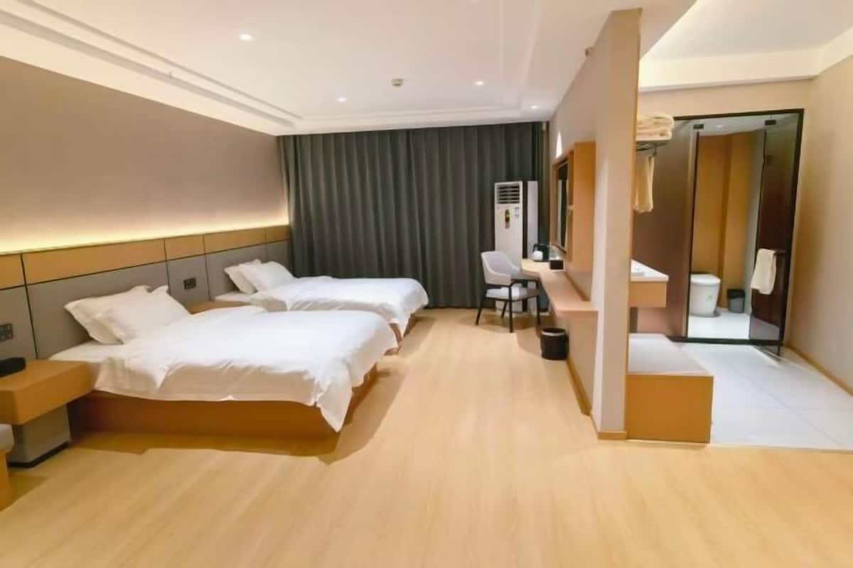 A hotel room with two beds, a desk, a chair, a mirror, and a bathroom visible through an open door.