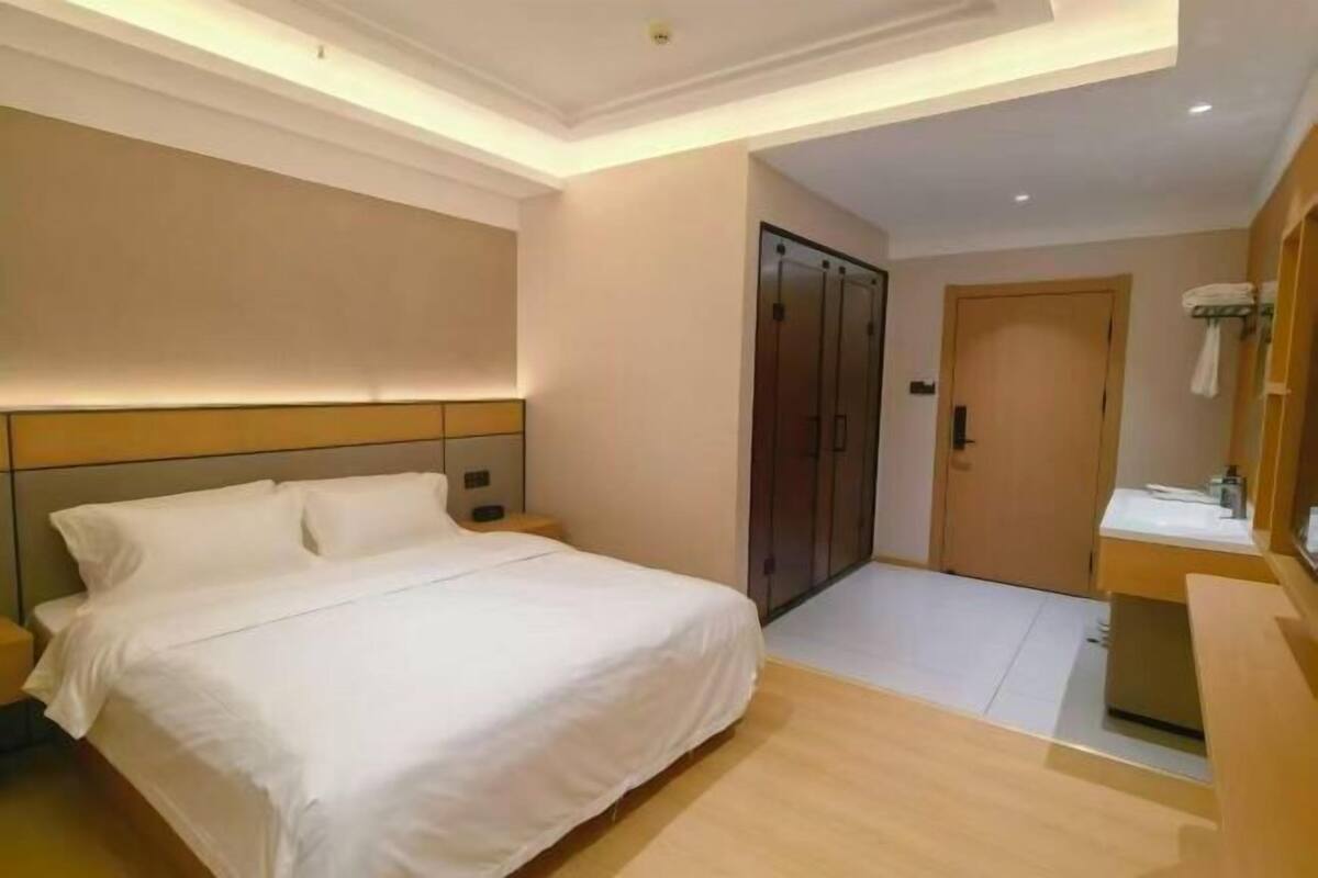 A hotel room with a bed, a wardrobe, a bathroom with a mirror, and a small seating area.