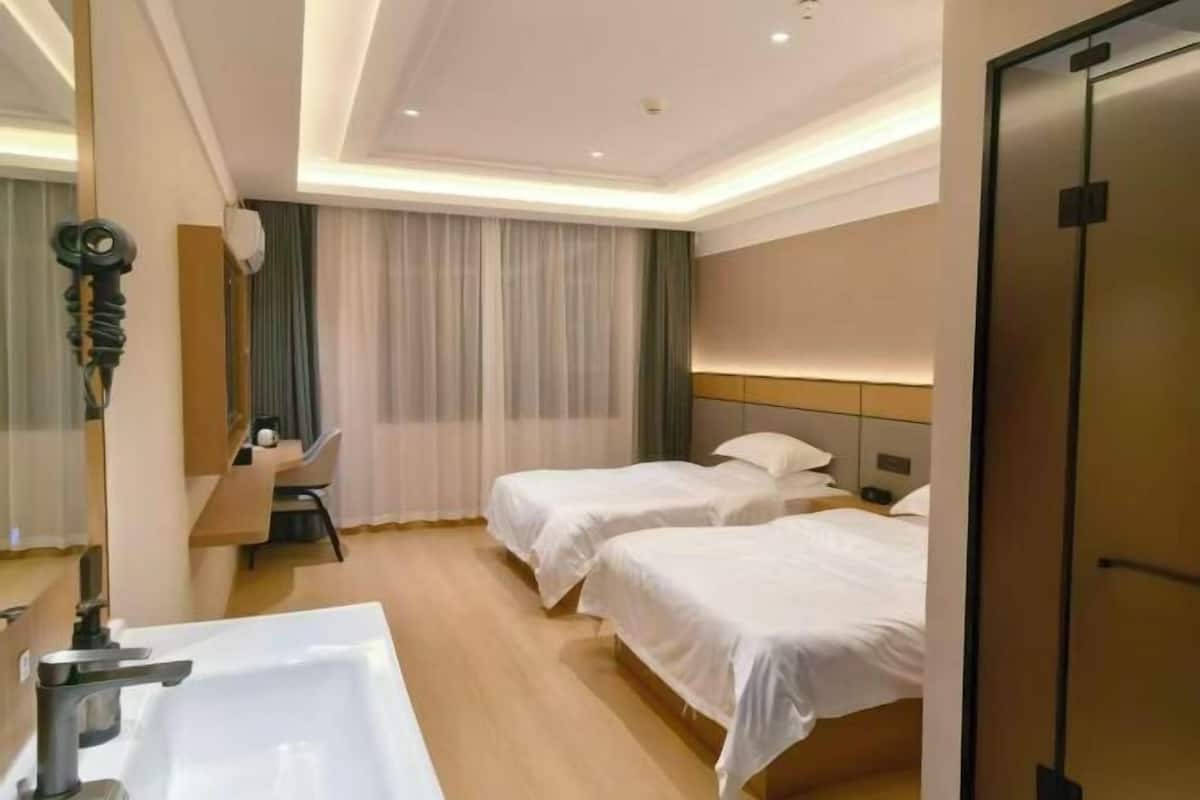A hotel room with two beds, a bathroom with a sink, and a desk with a chair.