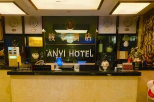 Un mostrador de recepción con una pantalla digital, un reloj y un cartel que dice 'ANYI HOTEL'.
