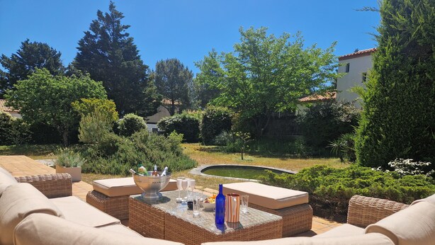 An outdoor seating area with wicker furniture, a table with a drink bowl, and a view of a garden and building in the background. - Rental House La Tranche-sur-Mer à La Grière - 50m from the beach - 14 people (La Tranche-sur-Mer)