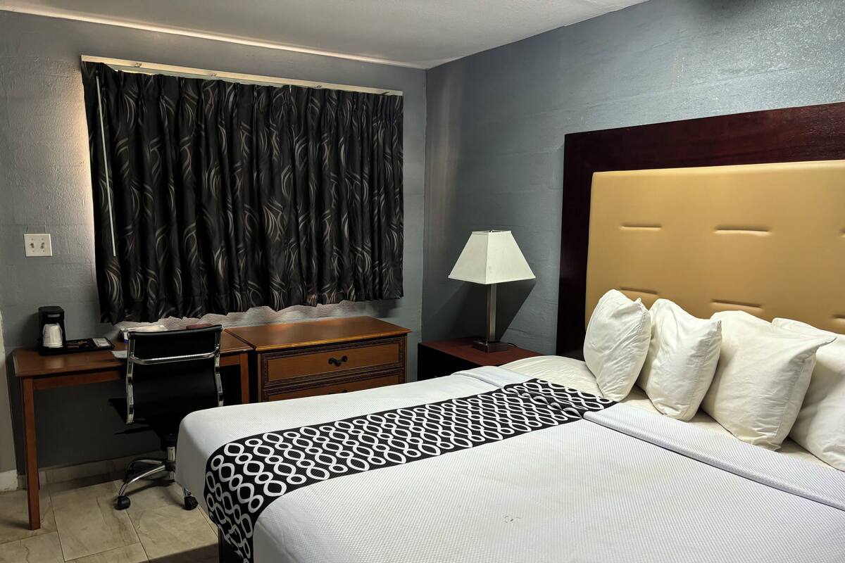 A hotel room with a bed, a desk with a chair, a lamp, and a coffee maker.